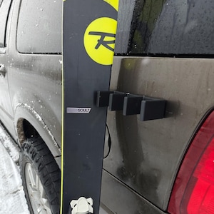May include: A black and yellow ski with the word "Soul7" printed on it. The ski is attached to a car with a black ski rack.
