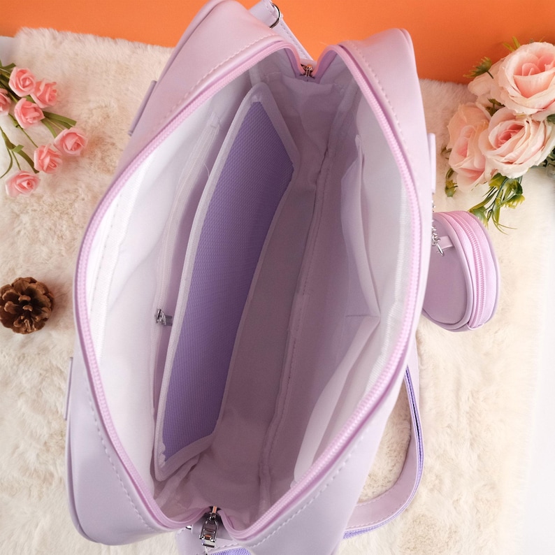 Puede incluir: Un bolso de mano de color lavanda con cierre de cremallera y una peque&ntilde;a bolsa redonda de color lavanda unida a &eacute;l. El bolso est&aacute; abierto y el interior est&aacute; forrado con una tela de color claro. El bolso tiene un bolsillo con cremallera en el interior.