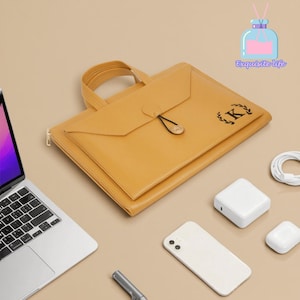 Peut inclure: Une serviette en cuir de couleur moutarde avec une poignée, une fermeture à bouton et la lettre "K" dans un motif de couronne. Un ordinateur portable, un téléphone, un chargeur et d'autres accessoires sont disposés autour de la serviette. Les mots "Exquisite Life" sont dans le coin supérieur droit.