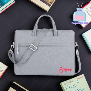 May include: Grey laptop bag with a shoulder strap and a zip closure. The bag has the name "Simona" embroidered on the front in red.