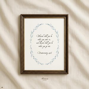 Pode incluir: Uma moldura de madeira castanho-escura contendo uma impressão branca com uma coroa de folhas em aguarela azul que rodeia o texto: Blessed shall you be when you come in, and blessed shall you be when you go out. Deuteronomy 28:6. A moldura tem um rebordo dourado.