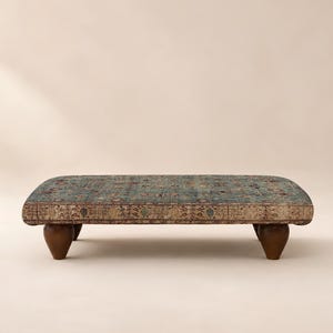 May include: A low rectangular ottoman featuring a blue and beige patterned textile top with intricate floral and geometric motifs. The piece is supported by four dark brown wooden legs that are rounded and tapered toward the base.