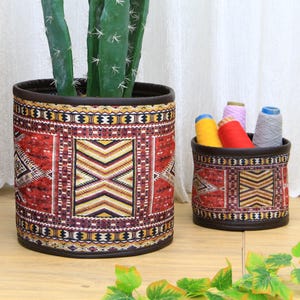 May include: Two cylindrical storage baskets with a colourful geometric pattern. The larger basket is filled with a cactus plant. The smaller basket is filled with colourful yarn.