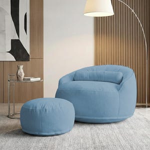 May include: A light blue corduroy beanbag chair with a matching ottoman. The chair has a rounded back and a cylindrical pillow. The ottoman is circular. The furniture is in a modern living room setting.