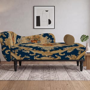 May include: A chaise lounge featuring a deep navy blue fabric upholstery with an intricate gold and cream-colored floral and scrollwork pattern. The piece is supported by four dark brown turned wooden legs and includes a small, solid tan bolster pillow.