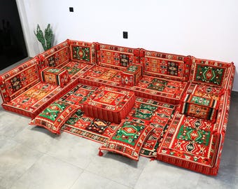 Puede incluir: Conjunto modular de asientos de suelo con un vibrante patrón geométrico rojo, verde y dorado. El conjunto incluye cojines, respaldos y un otomán central. El diseño presenta detalles intrincados y una estética tradicional, adecuado para salones o lounges.