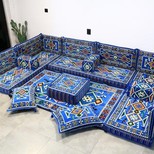 Puede incluir: Un conjunto de asientos modulares azules con un patrón geométrico. El conjunto incluye varios cojines y elementos de asiento en el suelo, creando un espacio habitable cómodo y elegante. El diseño incorpora tonos azules, naranjas y verdes.