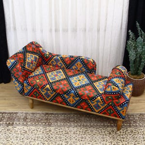 Puede incluir: Una chaise longue con estampado colorido y patas de madera. La chaise longue tiene un diseño geométrico con colores rojo, azul, amarillo y negro.