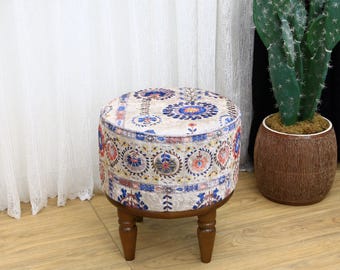 Könnte beinhalten: Ein runder, gemusterter Hocker mit beigefarbenem Hintergrund und blauen, roten und gelben floralen Mustern. Der Hocker hat vier Holzbeine.