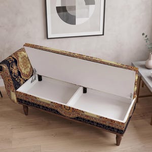 May include: A storage bench with a hinged lid that opens to reveal two white interior compartments. The exterior is upholstered in a dark blue and gold fabric featuring an intricate, ornate pattern. The bench stands on four dark wooden legs.
