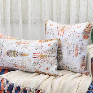 May include: Two decorative throw pillows with a white background and a colorful floral pattern. The pillows are on a couch with a multi-colored striped fabric and a white throw blanket.