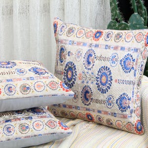 Puede incluir: Tres almohadas decorativas con fondo crema y un patrón floral azul y rojo. Las almohadas están dispuestas en un sofá de rayas crema y amarillo.