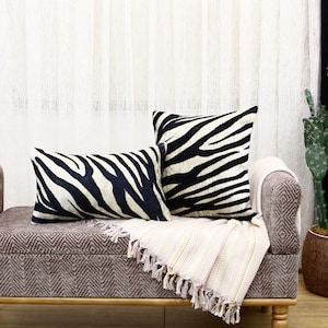 May include: Two decorative throw pillows with a black and white zebra print pattern. The pillows are on a brown couch with a white throw blanket.