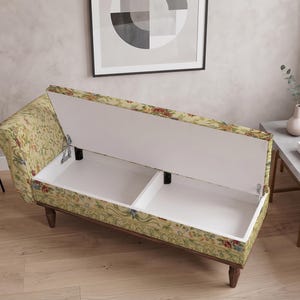 May include: A chaise lounge with a floral patterned fabric in shades of yellow, green, and red. The seat lifts to reveal two white storage compartments inside. The furniture features a curved backrest and dark brown wooden legs on a floor.