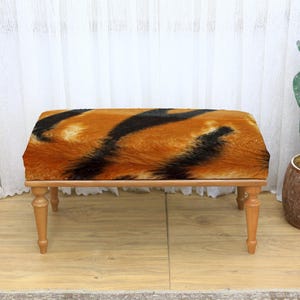 May include: A rectangular bench with a tiger stripe pattern in shades of orange, brown, and black. The bench has four wooden legs and a plush, textured seat. The bench is a decorative furniture piece.