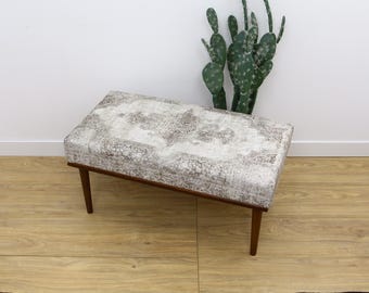 Puede incluir: Un banco con estampado blanco y marrón con patas de madera. El banco está sobre un suelo de madera marrón claro.