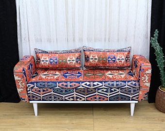 Könnte beinhalten: Ein weißes Sofa mit gemustertem Stoffbezug. Das Sofa hat zwei Kissen mit dem gleichen Muster. Das Sofa steht auf einem Holzboden.