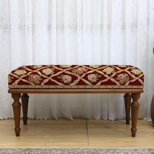 Puede incluir: Banco rectangular tapizado con un estampado floral en rojo, crema y dorado. El banco tiene un marco de madera y cuatro patas torneadas. El banco mide aproximadamente 91 cm de largo.