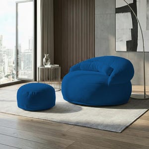 Pode incluir: Um conjunto de sala de estar moderno com uma grande poltrona azul redonda e um pufe a condizer. Os m&oacute;veis t&ecirc;m uma textura de veludo cotel&ecirc;. A sala tem uma janela grande, uma mesa lateral e um tapete cinzento.
