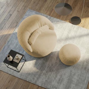 Pu&ograve; includere: Una poltrona in velluto a coste beige con poggiatesta attaccato e un pouf rotondo abbinato. La poltrona e il pouf sono su un tappeto azzurro, con un tavolino nero e oggetti decorativi. La stanza ha pavimenti in legno.