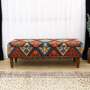 May include: A colorful patterned storage bench with a wooden frame and four legs. The bench has a geometric design with red, yellow, blue, green, and black colors.