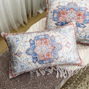 May include: Two decorative throw pillows with a white background and a colorful geometric pattern in shades of red, blue, and yellow. The pillows have a fringe trim.