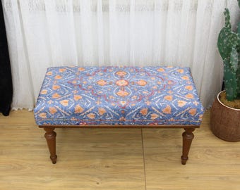 May include: A blue and orange patterned ottoman with wooden legs. The ottoman is sitting on a wooden floor.