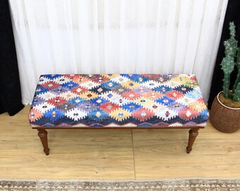 Puede incluir: Un banco de colores con un patrón geométrico en tonos azules, rojos, amarillos y blancos. El banco tiene un marco y patas de madera.