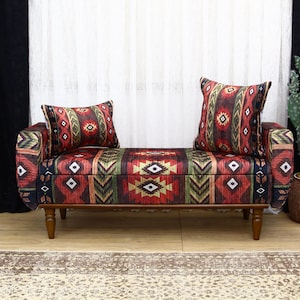 May include: A bench with a storage compartment and two matching throw pillows. The bench and pillows feature a colorful geometric pattern in red, green, and brown. The bench has wooden legs and is placed in front of a white curtain.