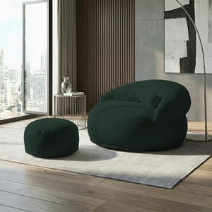 Pode incluir: Um conjunto de poltrona e pufe a condizer, verde escuro, com textura de veludo cotel&ecirc;. A poltrona arredondada tem um encosto baixo e um assento profundo. O pufe &eacute; circular e fica rente ao ch&atilde;o. O conjunto est&aacute; sobre um tapete cinzento claro.