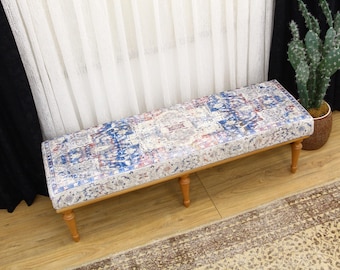 May include: A wooden bench with a patterned cushion. The cushion has a white background with blue, red, and pink geometric designs. The bench is sitting on a light brown rug.