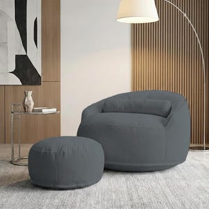 Pu&ograve; includere: Una poltrona a sacco in velluto a coste grigio con un pouf abbinato. La sedia ha una forma arrotondata con un poggiatesta integrato. Il pouf &egrave; circolare. L'arredamento &egrave; in un ambiente moderno.