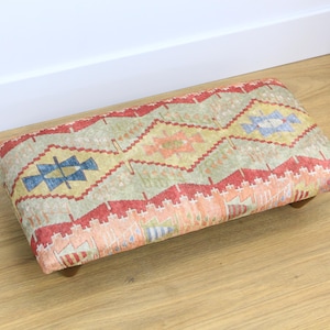 May include: A rectangular footstool with a colorful patterned fabric top. The fabric features a geometric design with shades of red, orange, yellow, blue, and green.