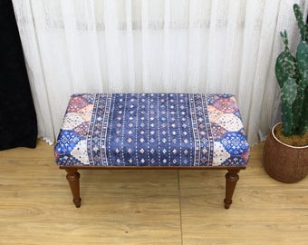 May include: A blue and white patterned bench with wooden legs. The bench is sitting on a wooden floor.
