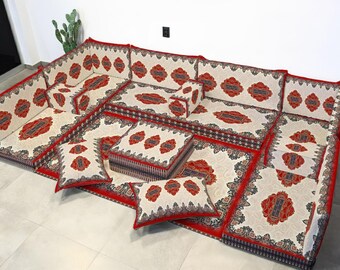 Può includere: Un set di sedute modulari da pavimento con sfondo color crema e motivi rossi e neri. Il set comprende più cuscini e cuscini, creando una seduta confortevole ed elegante. Progettato per l'uso a pavimento.