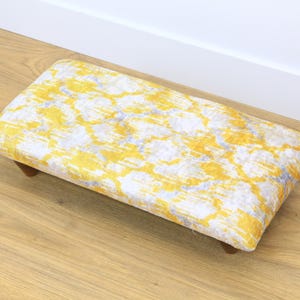 May include: A yellow and white patterned footstool with wooden legs.