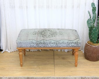 May include: A rectangular ottoman with a light blue and gray patterned top and four wooden legs. The ottoman's fabric features a central medallion design and decorative border. The legs are a light brown color.