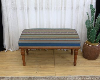 May include: A rectangular upholstered bench with a multi-colored striped pattern on the seat. The bench has a dark blue border and sits on four wooden, turned legs. The bench is approximately 36 inches long.