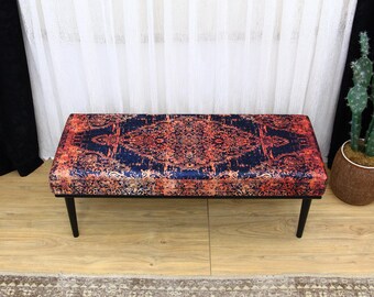 Könnte beinhalten: Eine dekorative Bank mit einer bunten, gemusterten Stoffoberfläche und schwarzen Metallbeinen. Der Stoff zeigt ein rotes, oranges und blaues Design mit filigranen Details.