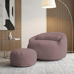 May include: A mauve corduroy beanbag chair with a matching cylindrical pillow and a round ottoman. The chair and ottoman are on a light gray rug. A modern floor lamp and side table are in the background.