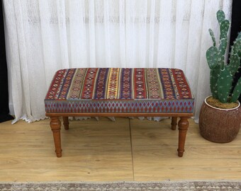 May include: A rectangular wooden bench with a patterned cushion. The cushion features a repeating design of red, blue, and gold geometric shapes. The bench has four turned legs and is approximately 36 inches long.