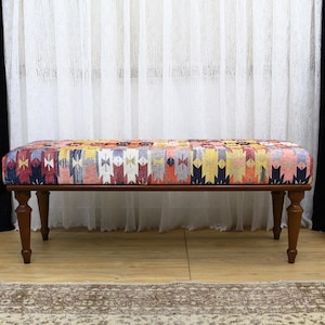 Può includere: Una panca in legno con un cuscino a motivi colorati. La panca ha gambe in legno tornite ed è appoggiata su un pavimento in legno.