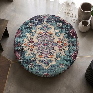 May include: A circular area rug featuring a distressed pattern in shades of teal, deep blue, cream, and accents of orange and purple. The rug displays a central medallion design with intricate floral and geometric motifs across its surface.