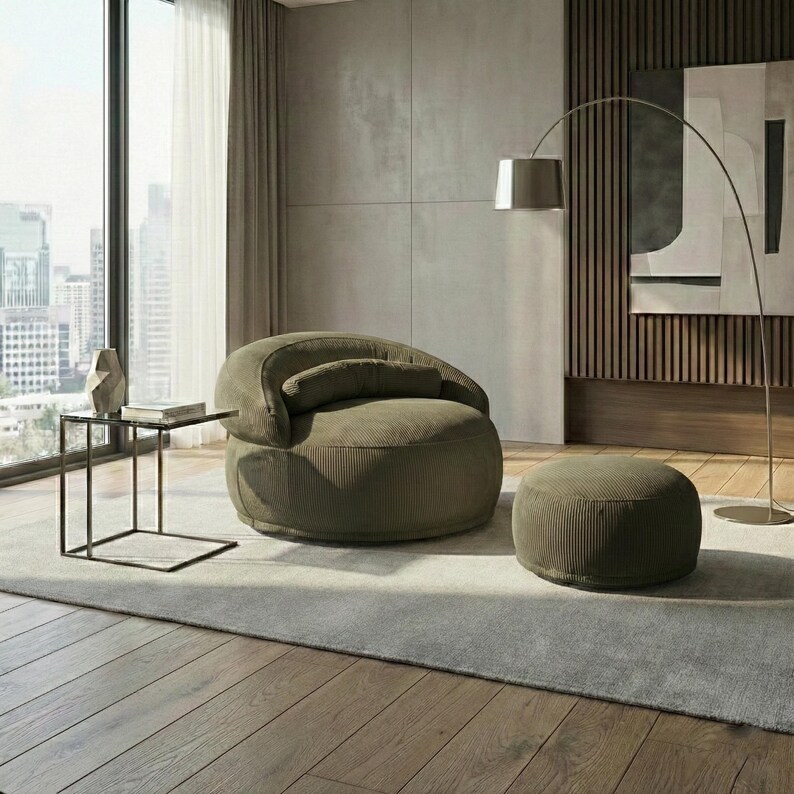 May include: An olive green corduroy armchair and ottoman set. The rounded armchair has a curved back and a small, attached pillow. The ottoman is circular. A modern floor lamp and side table are also in the room. The room has a neutral color palette.