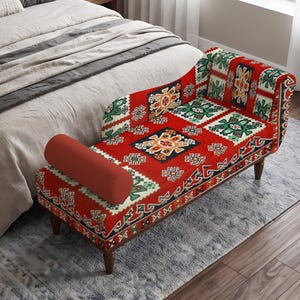 May include: A chaise lounge featuring a vibrant red fabric upholstery with a repeating geometric pattern in green, black, white, and orange. The piece includes a solid red cylindrical bolster pillow and is supported by four dark brown wooden legs.