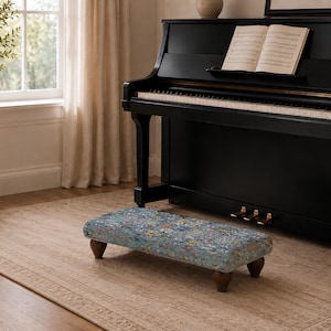Peut inclure: Un repose-pieds de piano rectangulaire doté d'un revêtement en tissu à motifs floraux bleus et multicolores. Le repose-pieds est soutenu par quatre pieds courts en bois brun foncé au design arrondi et effilé, offrant une base stable.