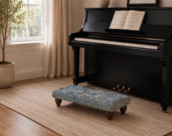 May include: A rectangular piano footstool featuring a blue, multi-colored floral patterned fabric upholstery. The footstool is supported by four short, dark brown wooden legs with a rounded, tapered design, providing a stable base for use.