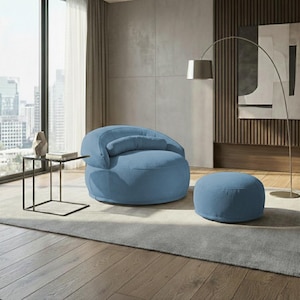 Pu&ograve; includere: Una poltrona in velluto a coste blu chiaro con un pouf abbinato. La sedia arrotondata ha uno schienale curvo e un piccolo cuscino attaccato. Il pouf &egrave; circolare. I mobili sono in un soggiorno moderno.