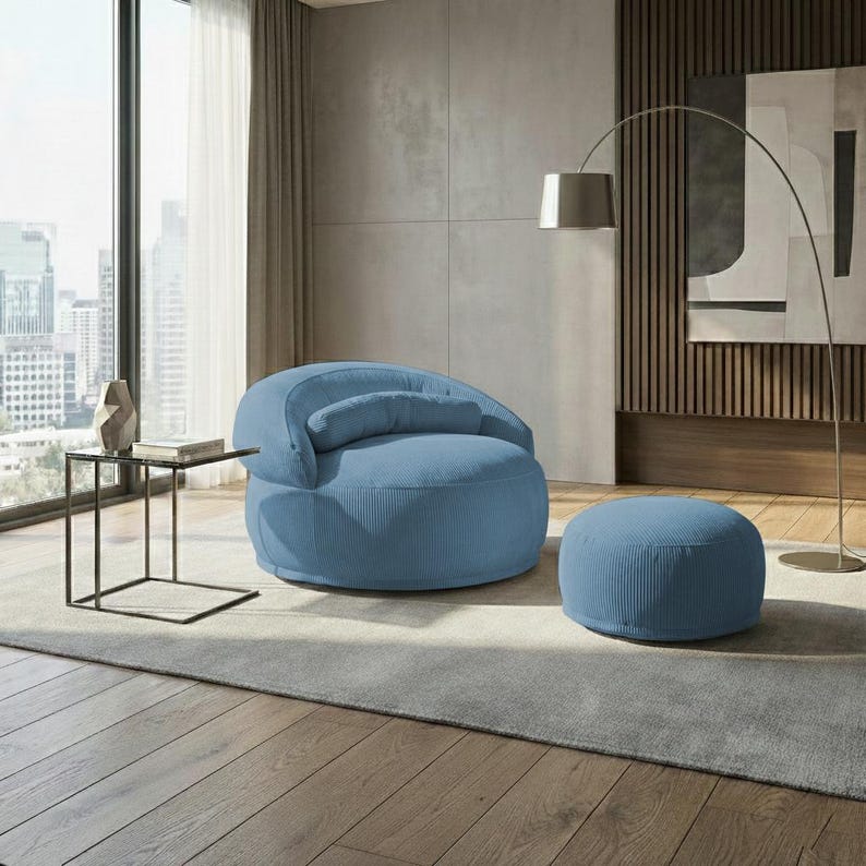 Pu&ograve; includere: Una poltrona in velluto a coste blu chiaro con un pouf abbinato. La sedia arrotondata ha uno schienale curvo e un piccolo cuscino attaccato. Il pouf &egrave; circolare. I mobili sono in un soggiorno moderno.
