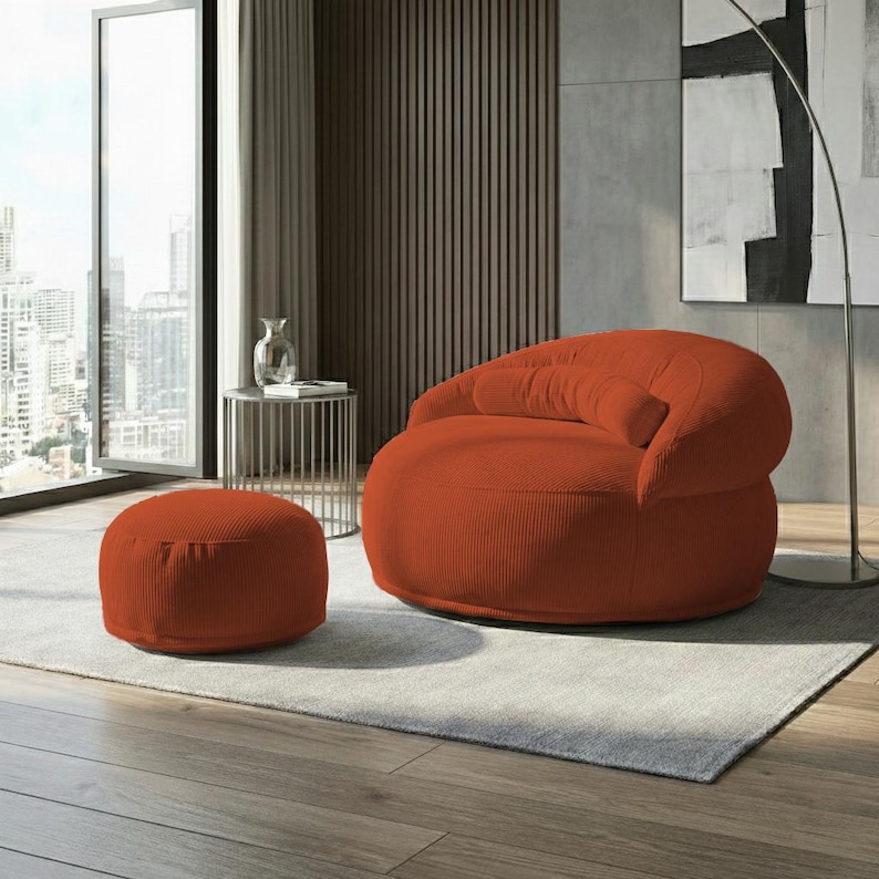 May include: An orange corduroy armchair and matching ottoman set. The chair has a rounded shape with a curved back and armrests. The ottoman is a small, round footrest. The set is placed on a light gray rug.